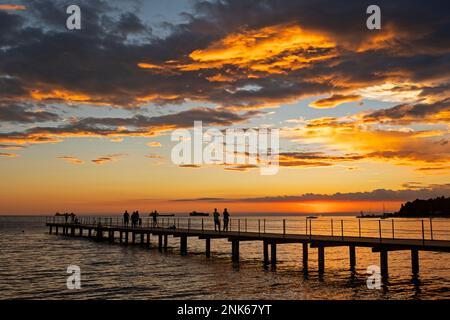 Anlegestelle mit Touristen, die vor dem Sonnenuntergang über der Adria in Ankaran an der slowenischen Riviera, Littoral-Region Sloweniens, stehen Stockfoto