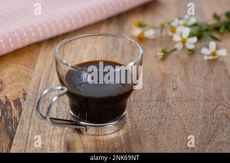 Ein Espresso in einem Glas auf einem Holztisch mit Wildblumen Stockfoto