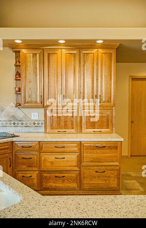 In dieser modernen Küchenumgestaltung sind Schranktüren aus Holz, Schubladen, Regale und eine Arbeitsfläche aus hellem Stein zu sehen. Stockfoto