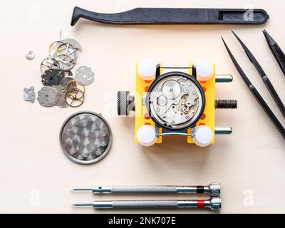 Ansicht von oben: Offene Uhr in gelbem Halter und Werkzeuge auf Holztisch in Uhrmacherwerkstatt Stockfoto