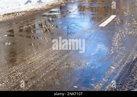 Pfützen aus geschmolzenem Schnee auf der Oberfläche von städtischen Asphaltstraßen am sonnigen Wintertag Stockfoto