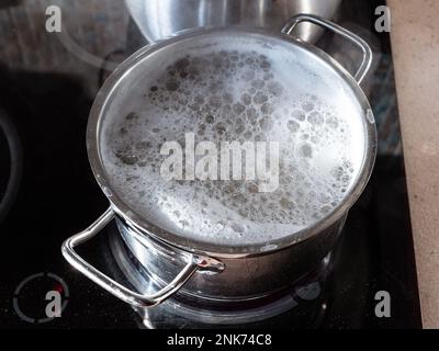 Nudelkochen in einer Stahlpfanne auf einem Keramikherd in der Küche Stockfoto