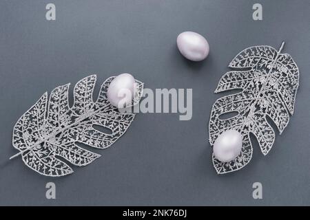 Silberne Eier, Monstera-Blätter von Draht auf grauem Hintergrund. Stockfoto