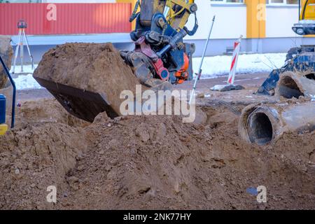 Ein Hydraulikbagger arbeitet auf einer Baustelle, um eine Rohrleitung im Winter zu ersetzen. Graben Sie Löcher für die Verlegung neuer Rohre für die Zentralheizung in einem Wohnhaus Stockfoto