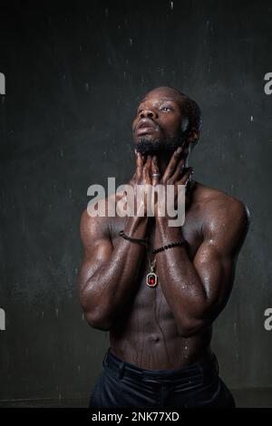 Fit für einen kräftigen jungen afroamerikanischen Mann, der unter dem Regen in der Nähe einer grauen Betonwand tanzt. Street Style-Konzept. Kopieren Sie den Speicherplatz zurück Stockfoto
