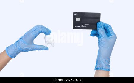 Zahnarzthelferin in blauen Handschuhen hält Zahnarztmodell und Kreditkarte. Heller Hintergrund. Kostenkonzept zahnärztlicher Behandlung Stockfoto