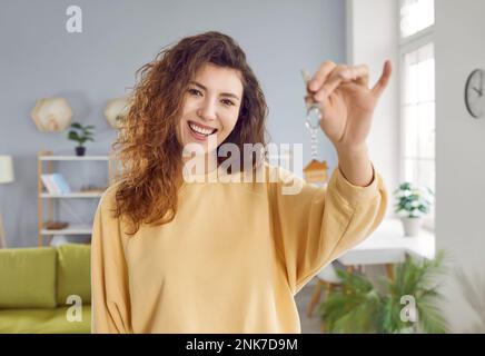 Porträt einer jungen, glücklichen, lächelnden, hübschen Frau mit Schlüsseln in der Hand, die zu Hause steht. Stockfoto