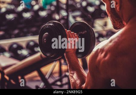 Bodybuilder trainiert mit Hanteln im Fitnessstudio. Ein Bodybuilder, der mit Kurzhanteln trainiert. Fitness-Mann, der Kurzhanteln hebt Stockfoto