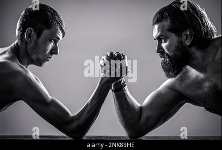 Arme mit dünner Hand, großer, starker Arm im Studio. Kräftig muskeliger, bärtiger Arm, der mit einem schwachen Mann kämpft. Schwarz auf Weiß Stockfoto