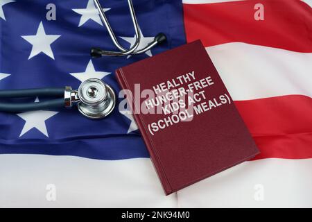 Regelkonzept. Auf der US-Flagge liegt ein Stethoskop und ein Buch mit der Inschrift - GESUNDE HUNGERFREIE KINDER ACT - SCHULMAHLZEITEN Stockfoto