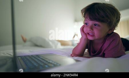 Ein Junge, der nachts im Bett liegt und Medienunterhaltung auf einem Laptop-Bildschirm anbietet. Ein hypnotisiertes Kind starrt abends auf einen blau leuchtenden Bildschirm Stockfoto