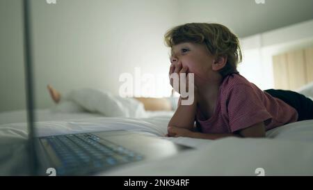 Ein Junge, der nachts im Bett liegt und Medienunterhaltung auf einem Laptop-Bildschirm anbietet. Ein hypnotisiertes Kind starrt abends auf einen blau leuchtenden Bildschirm Stockfoto