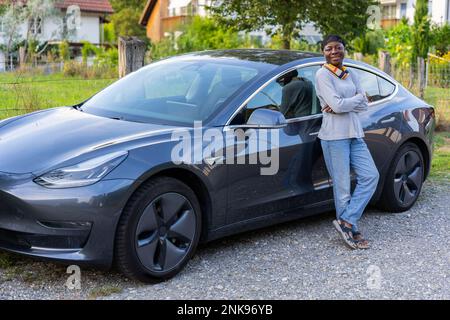 Seitenansicht einer glücklichen Afrikanerin, die vor ihrem Auto steht. Stockfoto