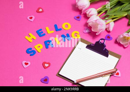 Komposition mit leeren Wörtern Hello Spring und wunderschönen Tulpenblüten auf pinkfarbenem Hintergrund Stockfoto