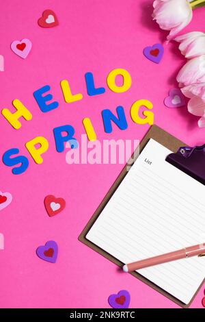 Komposition mit leeren Wörtern Hello Spring und wunderschönen Tulpenblüten auf pinkfarbenem Hintergrund Stockfoto