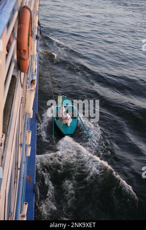 Männer, die Touristenschmuck und Textilgeschenke von einem kleinen Boot aus verkaufen, das an ein Kreuzfahrtschiff auf dem Nil gebunden ist Stockfoto