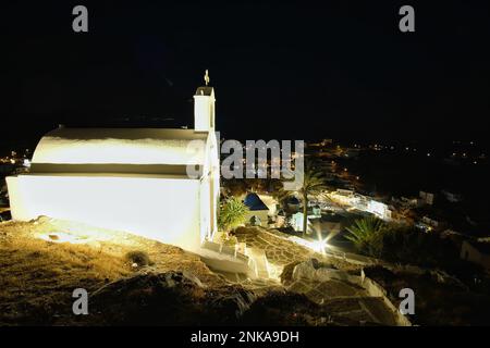 Blick auf eine kleine, beleuchtete, weiß getünchte Kirche in iOS Griechenland auf dem Gipfel des Hügels Stockfoto