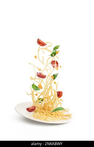 Pasta mit Tomaten und Basilikum, die in einen Teller fallen, Schweben. Stockfoto