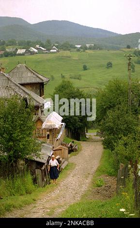 Unbefestigte Straße, die an einem großen Holzhaus in Solonetu Nou, Suceava County, Rumänien, 2001 vorbeiführt Stockfoto