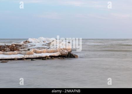 Nahaufnahme des eisigen Meeres, gefrorene Wellen, Felsen und Sonnenblendung auf dem Eis. Stockfoto