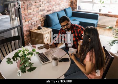 Ernsthafte Ehefrau und Ehemann planen Budget, prüfen Finanzen, fokussierte junge Frau mit Online-Rechner und Zählen von Rechnungen oder Steuern, Mann mit Laptop Stockfoto