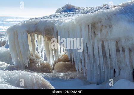 Nahaufnahme des eisigen Meeres, gefrorene Wellen, Felsen und Sonnenblendung auf dem Eis. Stockfoto