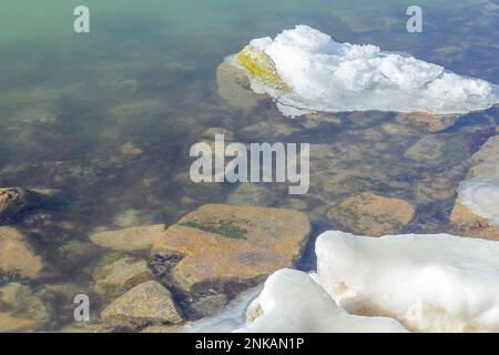 Nahaufnahme des eisigen Meeres, gefrorene Wellen, Felsen und Sonnenblendung auf dem Eis. Stockfoto