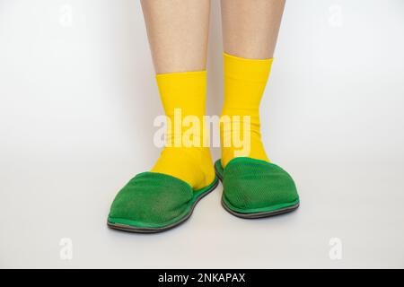 Frauenbeine in gelben Socken und grünen Hausschuhen auf weißem Hintergrund Stockfoto