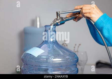 Nahaufnahme von weiblichen Händen, die an einer Wasserfüllstation Wasser in eine Flasche gießen Stockfoto