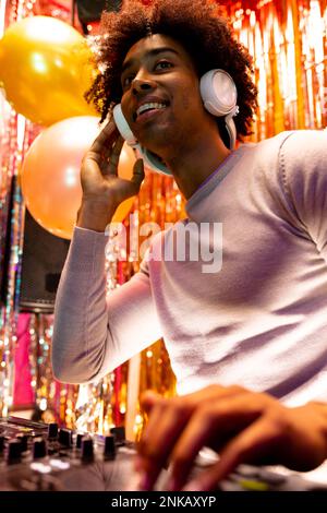 Vertikales Bild eines lächelnden afroamerikanischen djs in Kopfhörern, der in einem Nachtclub Musik spielt Stockfoto