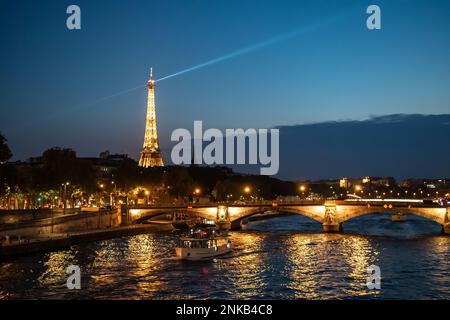 PARIS, Frankreich - 15. August 2022: Beleuchtete Brücke Pont des Invalides über der seine mit Tourbooten und Blick auf den Eiffelturm bei Nacht in Paris Stockfoto