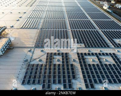 Große Solarpaneelanlage in einem gewerblichen Lagerhaus mit Blick auf den Sonnenuntergang aus der Vogelperspektive Stockfoto