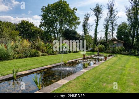 Sommerszene mit Blick auf einen Rasen mit einem Rasen in einem englischen Landgarten mit einem kleinen Springbrunnen und sanften Reflexionen Stockfoto