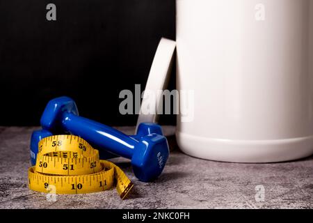 Nahaufnahme eines Molkenproteinpulvers, Kurzhanteln und Maßband isoliert auf schwarzem Hintergrund Stockfoto