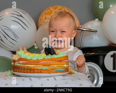 Ein einjähriger Junge sitzt an seinem ersten Geburtstag vor seinem Geburtstagskuchen und weint Stockfoto