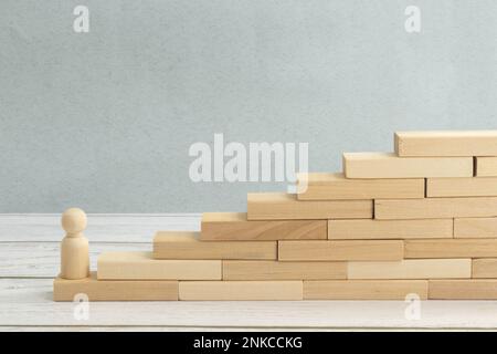 Auf der ersten Stufe steht die Holzfigur eines Mannes auf einer Treppe aus Blöcken. Das Konzept der Erreichung der gesetzten Ziele in den Bereichen Business, Career Growth, st Stockfoto