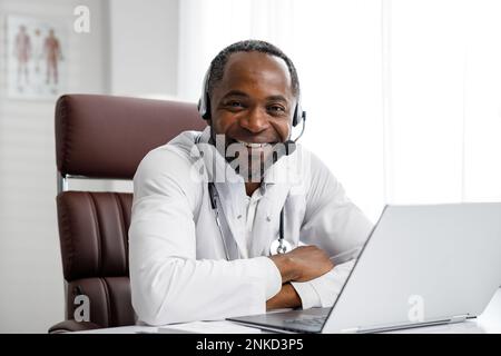 Ein afroamerikanischer Arzt begrüßt die Online-Patientenberatung auf dem Laptop. Ein Büro, das telemedizinische Dienste erbringt. Online-Medizin und Stockfoto