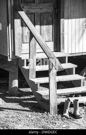 Ein schwarz-weißes Bild von einem Paar Arbeitsstiefel an der Seite der Treppe, die zur Tür einer Residenz, Roatan, Honduras, führt. Stockfoto