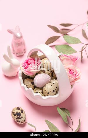 Korb mit Osterwachteleiern, Rosenblüten, Eukalyptusästen und Hasen auf rosa Hintergrund Stockfoto