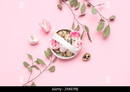 Korb mit Osterwachteleiern, Rosenblüten, Eukalyptusästen und Hasen auf rosa Hintergrund Stockfoto