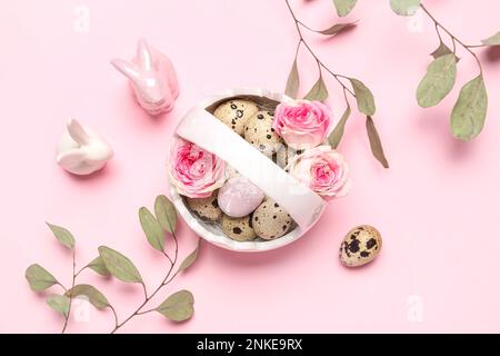 Korb mit Osterwachteleiern, Rosenblüten, Eukalyptusästen und Hasen auf rosa Hintergrund Stockfoto