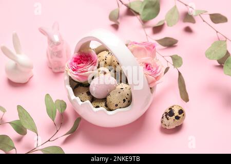 Korb mit Osterwachteleiern, Rosenblüten, Eukalyptusästen und Hasen auf rosa Hintergrund Stockfoto