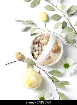 Korb mit Osterwachteleiern, Hähnchen, Kamillenblüten und Eukalyptuszweigen auf weißem Hintergrund Stockfoto