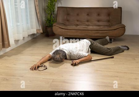 Asiatischer Senior-Mann fiel hinunter und lag auf dem Boden, während er zu Hause mit Gehstock spazieren ging. Stockfoto