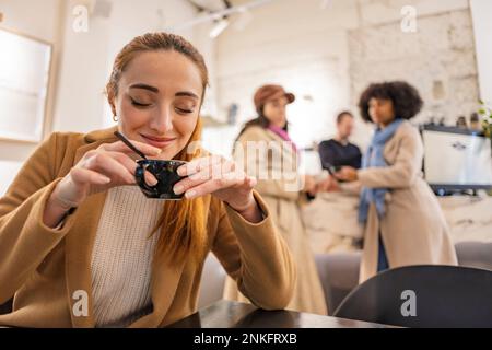Eine lächelnde Frau hält eine Kaffeetasse und Freunde stehen im Hintergrund Stockfoto