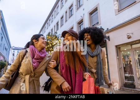 Glückliche multirassische Freunde, die mit Einkaufstaschen in der Stadt spazieren gehen Stockfoto
