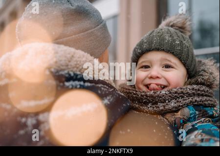 Vater trägt einen Jungen, der im Winter die Zunge herausstreckt Stockfoto