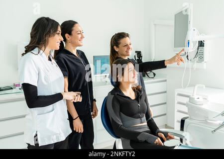 Glückliche Ärztinnen mit Patientin, die in der Klinik auf einem Stuhl sitzt Stockfoto