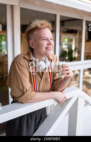 Lächelnde nicht-binäre Person mit Einweg-Kaffeetasse am Geländer Stockfoto