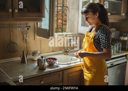 Junge Frau in gelber Schürze, die an der Küchentheke steht Stockfoto